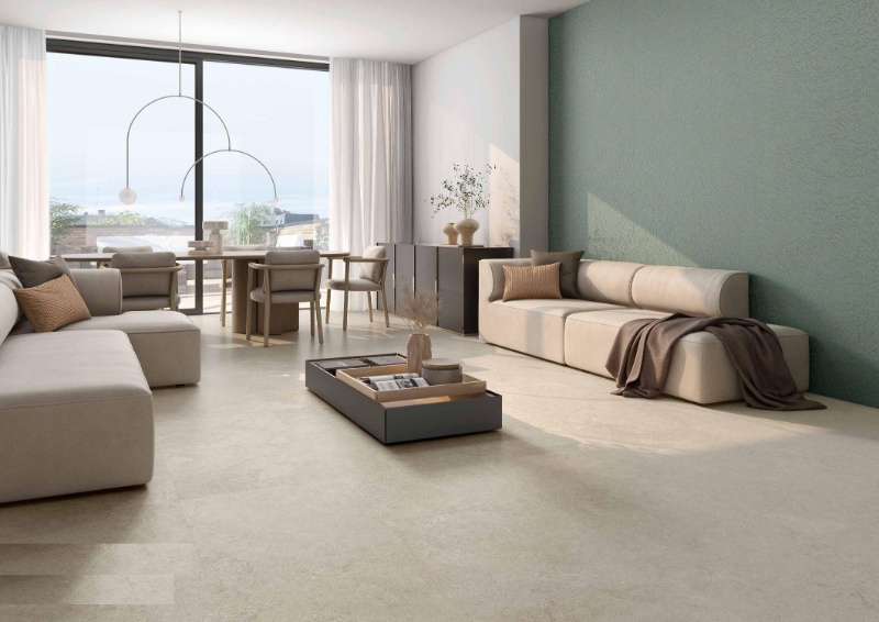 A luxury living room with cream marble-look floor tiles, sage green accents, walnut furniture and subtle brass details.